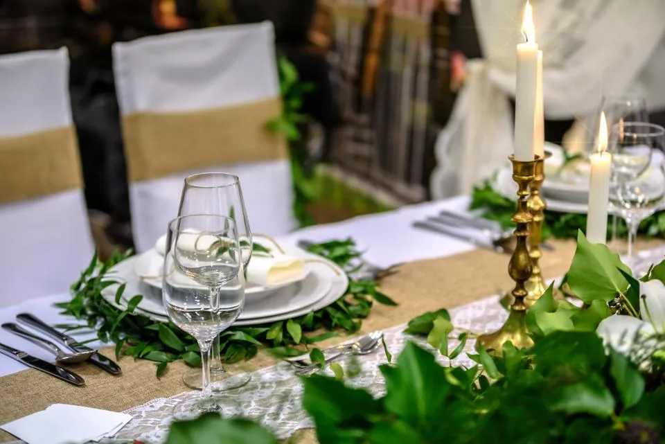 Mesa de evento preparada con candelabro dorado, copas, vajilla y un camino de hojas verdes