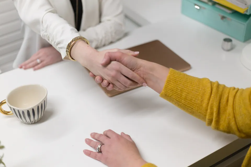 Dos personas se dan la mano sobre una mesa de trabajo